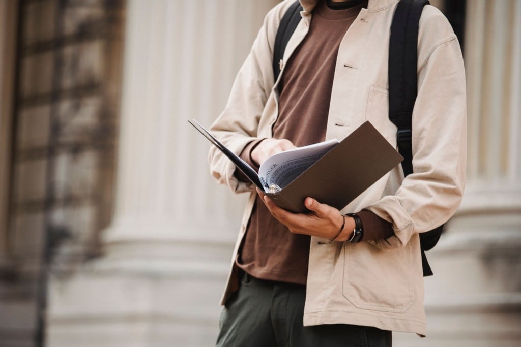 Cómo sacar el NIE en España siendo estudiante: pasos en 2026 Estudiante revisando documentos junto a un edificio universitario