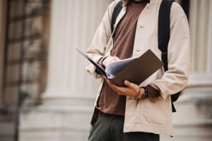 Estudiante revisando documentos junto a un edificio universitario